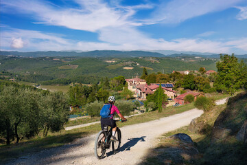 nice senior woman riding her electric mountain bike between olive and cypress trees in the Ghianti Area of Tuscany near Gaiole, Italy

