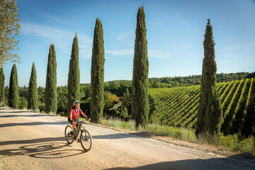 nice senior woman riding her electric mountain bike between olive and cypress trees in the Ghianti...