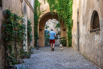 Uomo passeggia con il cane in un vicolo di un borgo medievale - obrazy, fototapety, plakaty
