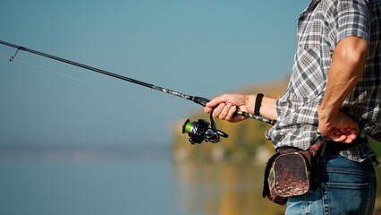 The hands of an adult mature man hold a fishing rod. Senior man spends time fishing on a warm sunny...
