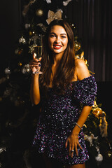 Portrait of a glamorous Caucasian woman in a shiny blue dress near a Christmas tree with a glass of champagne.New Year and Christmas concept