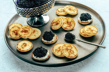Blinis with black caviar and cream cheese, on a festive dish, mini pancakes, an elegant appetizer
