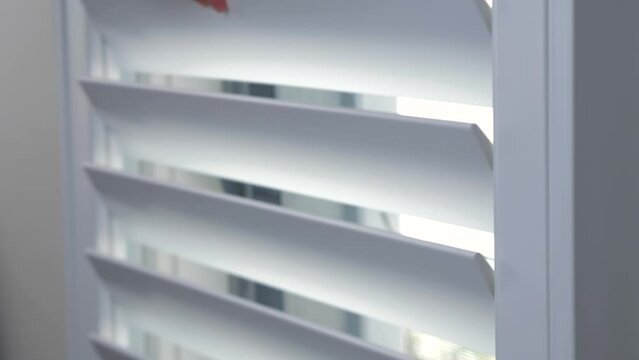 Close-up shot of Plantation Shutters window frame slats being closed with hands in house interior design wall kitchen privacy security protection 4K