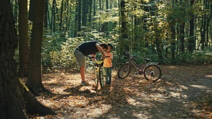 A father and son are repairing a bicycle in the forest. Time spent together with parents and children in nature on active recreation. A man teaches a boy to repair. High quality 4k footage