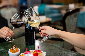Close up of hands young couple man and woman clinking with glasses of red and white wine at restaurant