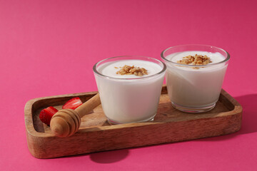 Bowls with yogurt on wooden stand on pink background