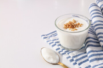 Glass with yogurt, towel and spoon on white background, space for text