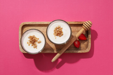 Bowls with yogurt on wooden stand on pink background, top view