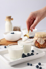 Bowls with yogurt, bottle with milk, jars and spoon in hand on white background