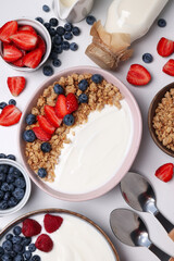 Bowls with yogurt and berries, spoons and bottle with milk on white background, top view
