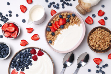 Bowls with yogurt and berries, spoons and bottle with milk on white background, top view