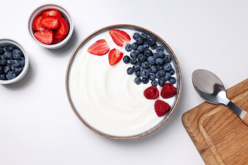 Bowls with yogurt and berries, spoon and board on white background, top view