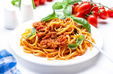 Spaghetti bolognese pasta with minced meat in tomato sauce with green basil leaves on white table background, top view