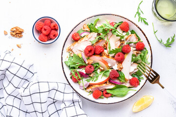 Fresh salad with raspberries, grilled chicken, pears, cheese, onion, walnuts, spinach and arugula, white table background, top view