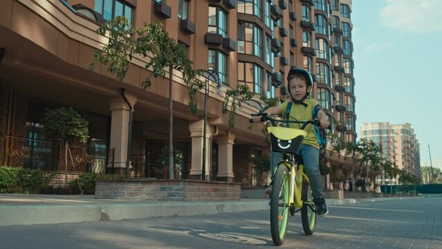 A child boy in a helmet rides a bicycle in a cityscape. Active recreation, happy childhood and speed. High quality 4k footage