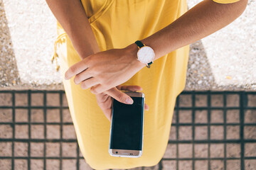 Troubled woman checking time on wristwatch while waiting for meeting and using smartphone on street