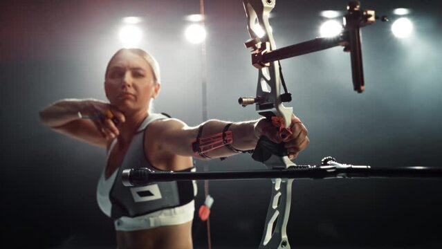 Professional Female Archer Aiming and Shooting at a Target with a Modern Compound Bow. Athlete is Fully Equipped and Protected with Chest and Arm Guards. Slow Motion Effect with Speed Ramping