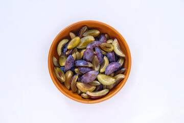 Sweet and ripe pieces of plums in a brown color clay bowl on white background.
