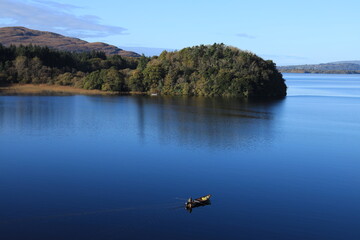 Landscape at Lough Gill, County Leitrim and County Sligo, Ireland featuring man fishing from small boat in still reflective waters on autumn day