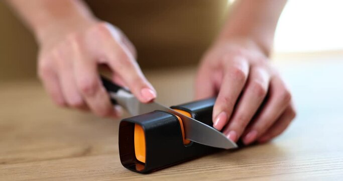 Women's hands on the table sharpen a knife with a sharpener, a closeup. Kitchen manual device, slowmotion