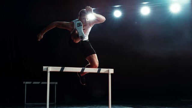 Strong Male Athlete is Running Towards an Obstacle, Hurdling, Jumping Over the Barrier at High Speed while Sprinting in a Race. Cinematic Super Slow Motion Footage with Speed Ramp Effect
