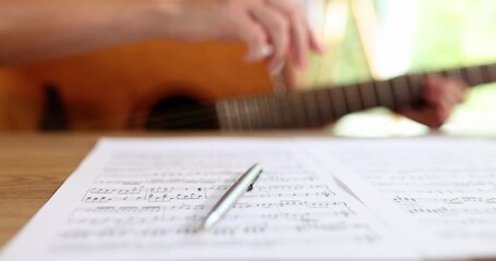 A woman with a guitar writes notes with a pen, close-up. The concept of learning solfeggio online, musical literacy