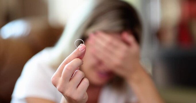 A crying woman holds a wedding ring, a close-up, shallow focus. Concept of family breakdown, treason