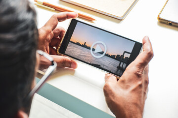 Person holding smartphone preparing to watch a beautiful sunset cityscape video. Play button, close up shot selective focus.