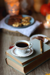 Cup of tea or coffee, plate with desserts, dried oranges, bowl of grapes, scented candles, vintage books, pumpkins and autumn leaves on the table. Autumnal hygge. Selective focus.