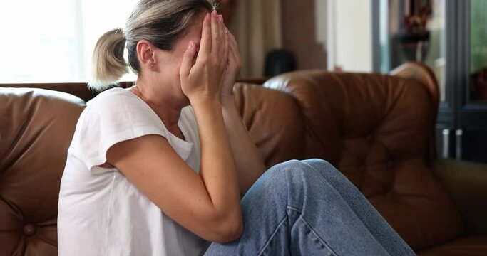 A woman sitting on the couch is bitterly crying, a close-up, slowmotion. Concept emotional suffering, grief