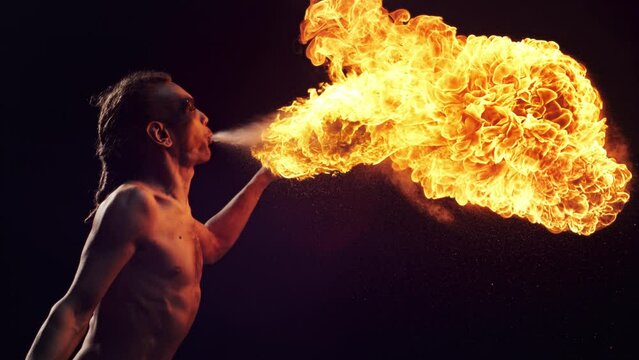 Fire Breather Performing at a Show on a Dark Stage. Male Performer Blowing Fire Out of His Mouth with Beautiful Visual Effect. Cinematic Super Slow Motion Footage with Speed Ramp Technique