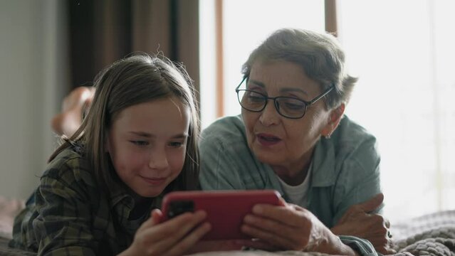 Grandma and granddaughter spending time together playing games on a mobile phone.
