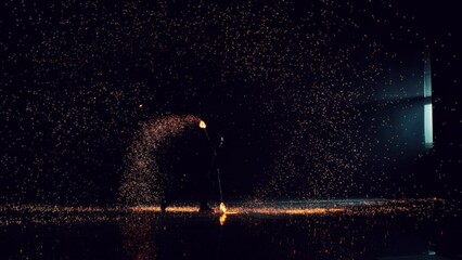Cinematic Super Slow Motion Footage with a Traditional Fire Performance. Silhouette of a Fire Dancer Spinning Fire Poi on a Dark Stage. Bright Hot Sparks Flying Around Across, Illuminating the Space