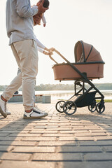 Side view. A young couple with a baby pram is walking together