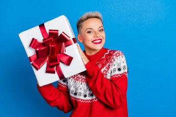 Photo of adorable positive pleasant girl with short hairstyle dressed red sweater hands hold gift box isolated on blue color background