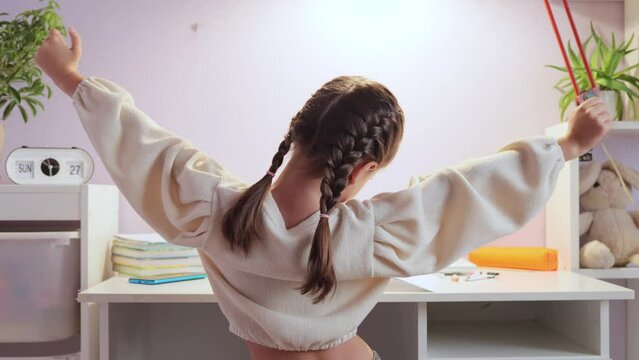 Cute little girl feeling tired while studying at table at home posing backwards stretching arms and sides after sitting in uncomfortable posture while doing homework.