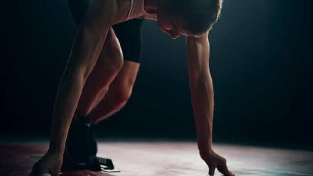 Strong Young Man Starting a Race From Track Starting Blocks Position on a Dark Stadium in the Evening. Cinematic Portrait of a Fit Male Sprint Runner Participating in a Competition