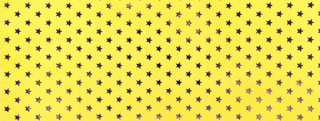 Golden background from metal foil paper with pattern of stars closeup. Texture of yellow metallized...