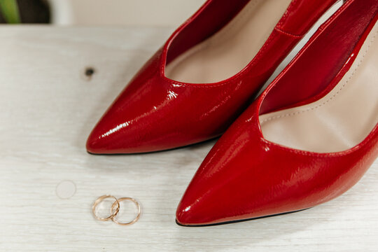 Red patent leather shoes of the bride near gold wedding rings