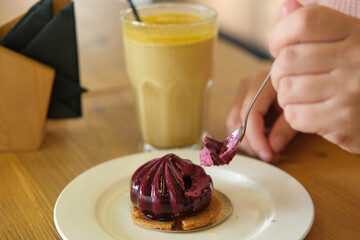 Woman eating delicious fresh blueberry mousse cake. Cutting dessert texture close up. Person taking bite slice of purple cheesecake in a restaurant, cafe. Spoon breaks off a piece of berry juicy cake