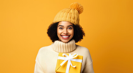 Pretty african american woman holding gift box in arms on yellow background. Happy smiling girl with christmas present in her hands