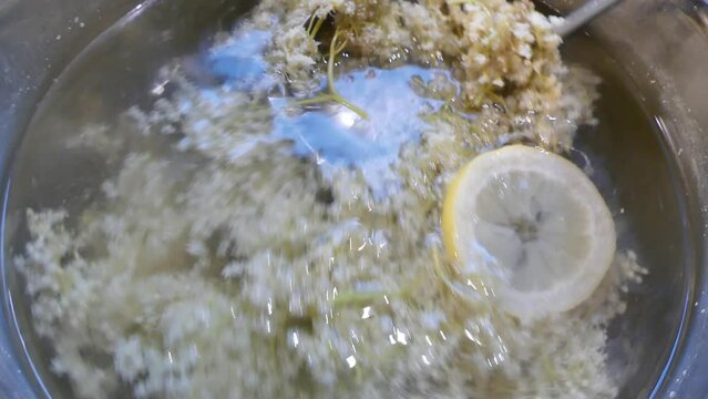 Water with elderberry flowers and slices of cut lemon, mixing with metal ladle in pot - preparation of healthy, natural homemade drink. Topics: natural vitamins, naturally immune drink, health
