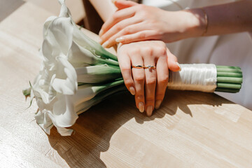 The bride's hands with an engagement ring lying on a bouquet of white calla lilies
