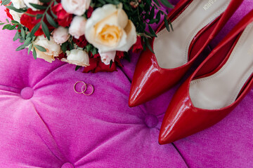 Red patent leather shoes of the bride near gold wedding rings and a bouquet of roses