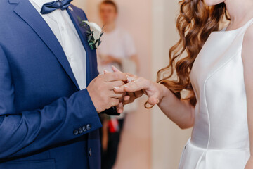 Groom putting golden ring on bride's finger during wedding ceremony. Hands with rings close up