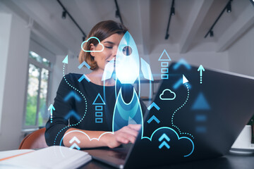 Pensive attractive beautiful businesswoman in formal wear working on laptop at office workplace in background. Concept of start up new business. Rocket icon hologram. Table, notebook.