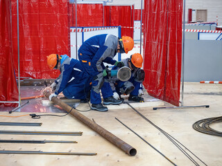 Workers saw pipes and fittings. Builders work inside hangar. Three workers with circular saw. Production of construction scaffolding. Process of creating mezzanine. Builders manipulating scaffolding