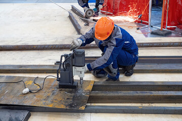 Man drills hole in metal. Worker in production facility. Man in helmet uses drilling machine. Process of drilling hole in metal beam. Master works with drilling equipment. Production, industrial