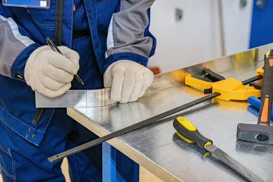 Worker makes mark on steel slat. Master marks place where iron bends. Metalworking in production. Hands near table with construction tools. Processing metal slat. Worker in gloves doing metalworking