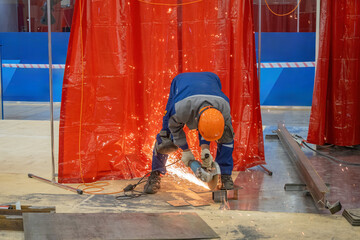 Man with hand-held circular saw. Builder saws off piece metal sheet. Master with circular saw in hangar. Man in helmet works with dangerous equipment. Builder with saw in production workshop